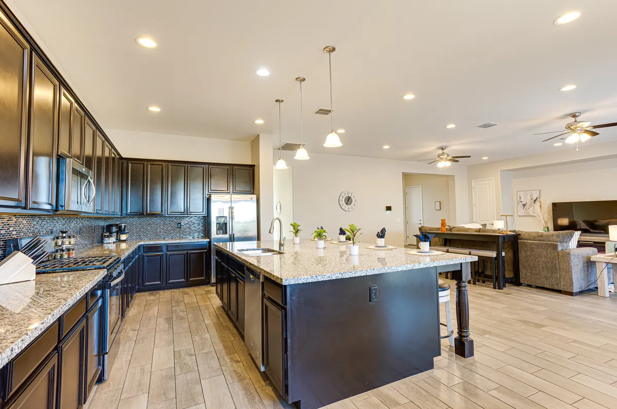 A close perspective on the kitchen island with a granite countertop, dark cabinetry, and an open layout. The image captures modern appliances and the sense of spaciousness. The kitchen is presented as both practical and inviting, ideal for cooking and entertaining.