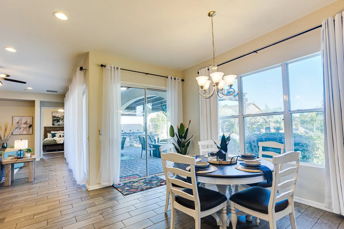 A bright, cheerful dining area set for a meal, featuring a dining table with place settings, overhead chandelier, indoor plants, and expansive windows that allow for ample natural light to fill the room.