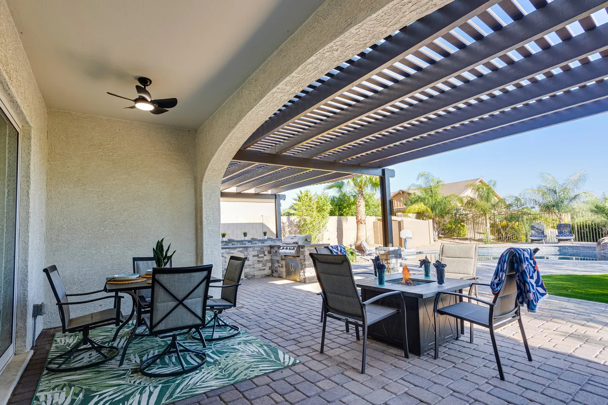 A stylish backyard with an alfresco dining area next to a shimmering swimming pool. The outdoor dining table is set, and a nearby grill station hints at the perfect spot for barbecues and evening gatherings. Lush landscaping frames the scene, enhancing the atmosphere of tranquility and comfort.