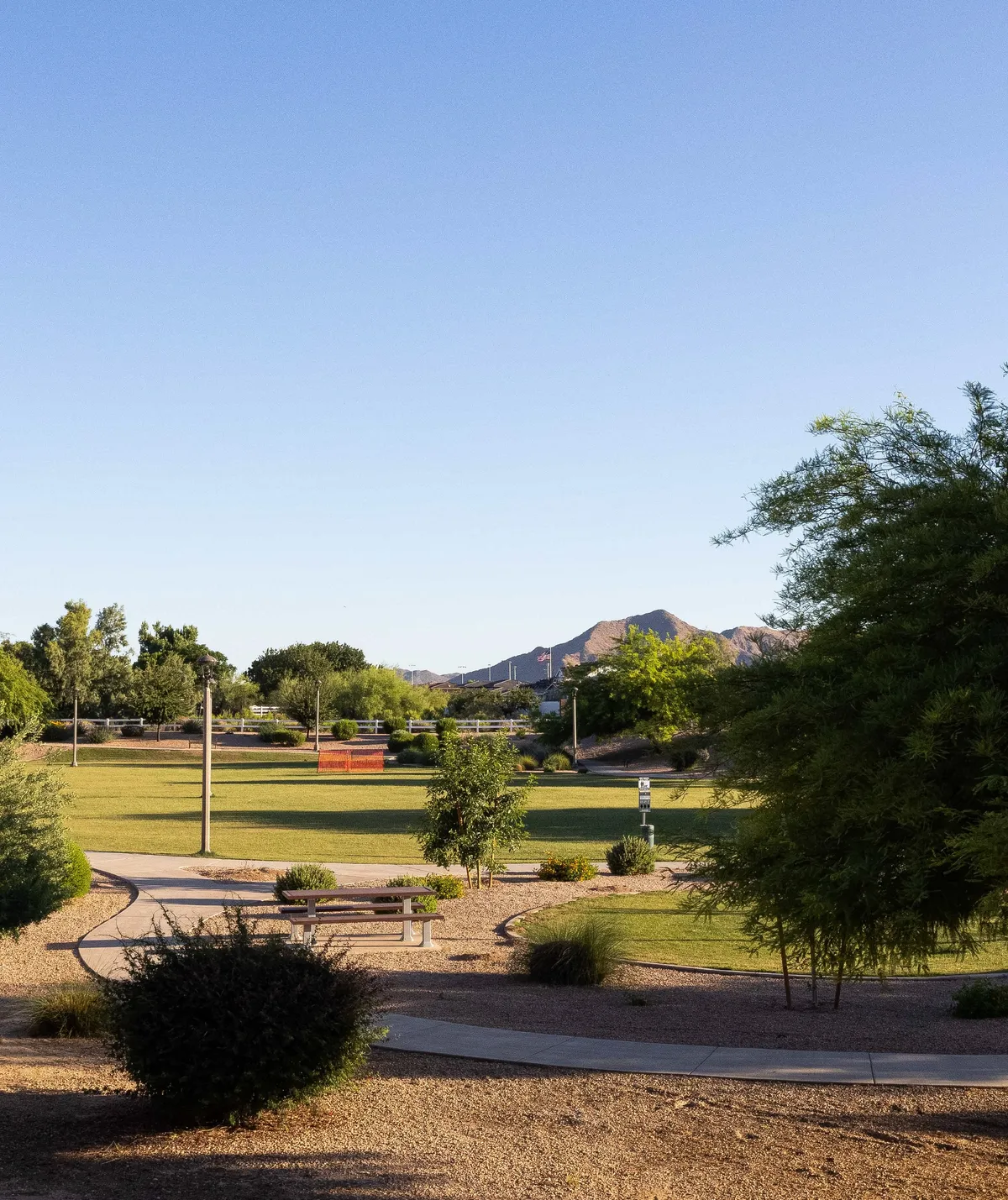 A lush green park area with a winding walking path, picnic bench, and beautiful mountain backdrop. The open grassy space is perfect for outdoor play and picnics, embodying the local parks mentioned in the section.