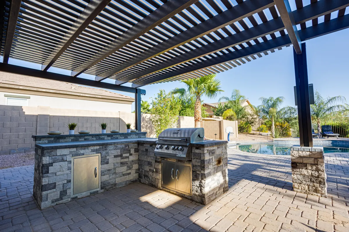 This photo showcases an expansive outdoor kitchen and grill area adjacent to a swimming pool, with palm trees creating a resort-like vibe. The space is tailored for entertaining guests, barbecuing, and poolside dining, especially at sunset.