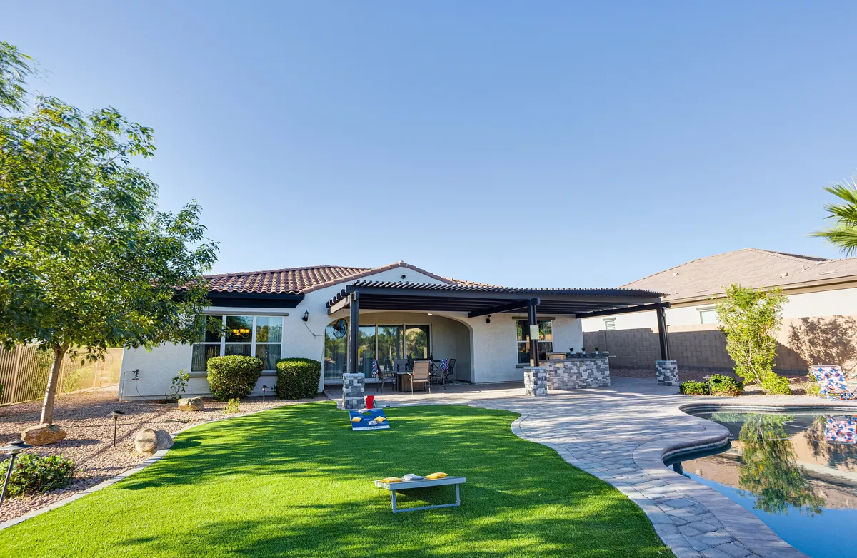 A relaxed backyard scene with a sparkling swimming pool, a manicured lawn area, comfortable patio seating, and mature landscaped trees. The setting is perfect for sunset pool parties, outdoor games, or simply unwinding in the evening with friends and family.