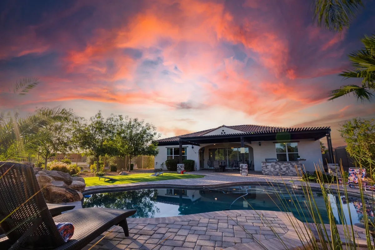 A tranquil backyard scene featuring a sparkling swimming pool at sunset, with the home's facade, green lawn, and a vibrant, colorful sky. The setup promises a peaceful atmosphere for poolside relaxation and gatherings.