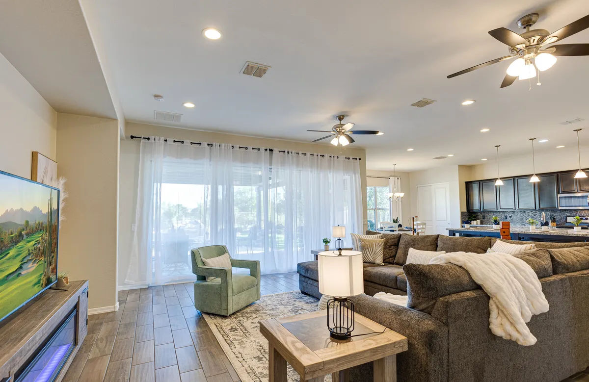 A welcoming living area with a large sectional sofa, coffee table, television, and a view into the open kitchen area. The space is filled with comfortable seating and is bathed in light from windows, reinforcing a sense of togetherness and relaxation.