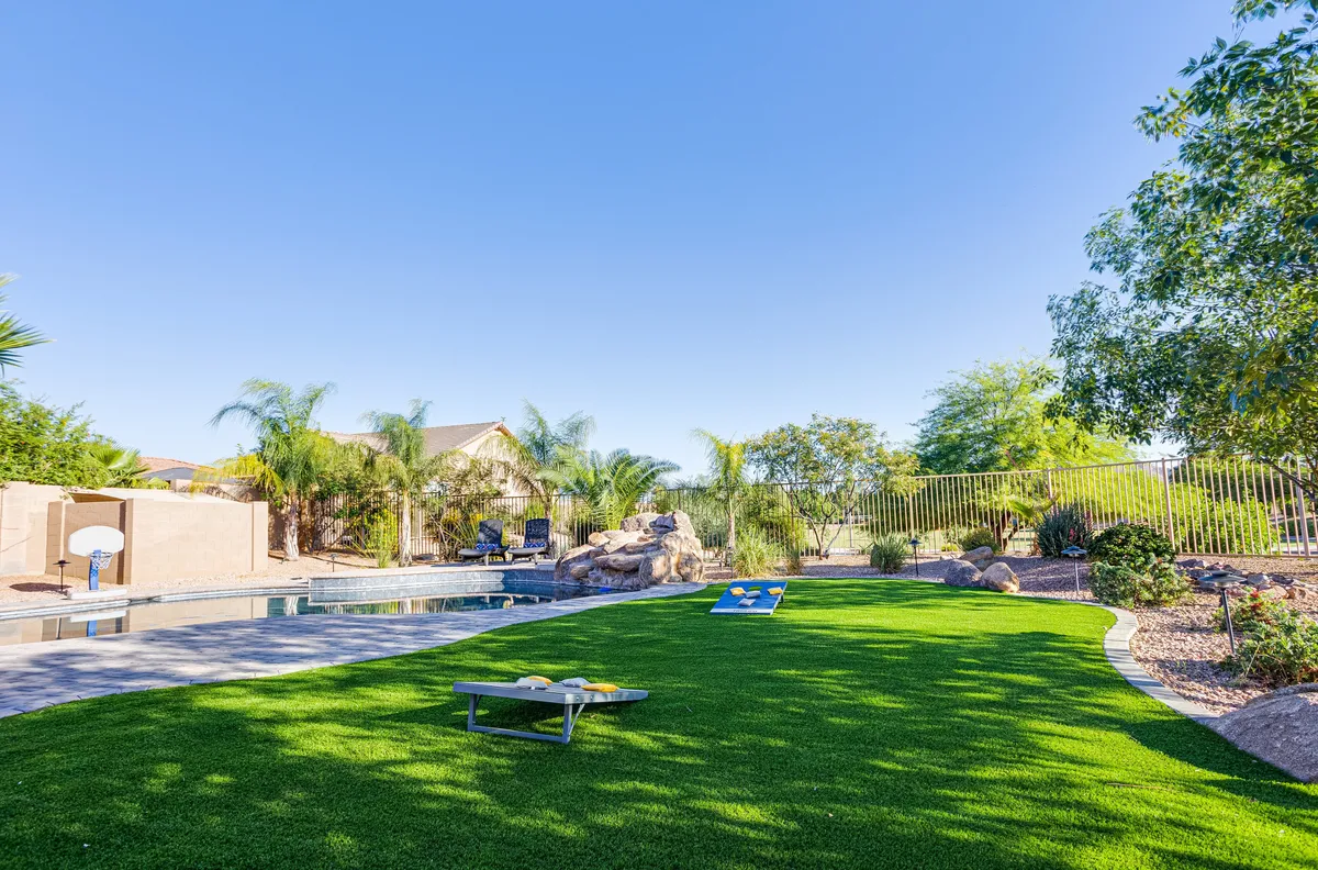 A vibrant backyard scene featuring a sparkling swimming pool, green lawn, comfortable seating area, and a basketball hoop. The playful setup includes space for swimming, sunbathing, and outdoor games, evoking a sense of family fun and relaxation.