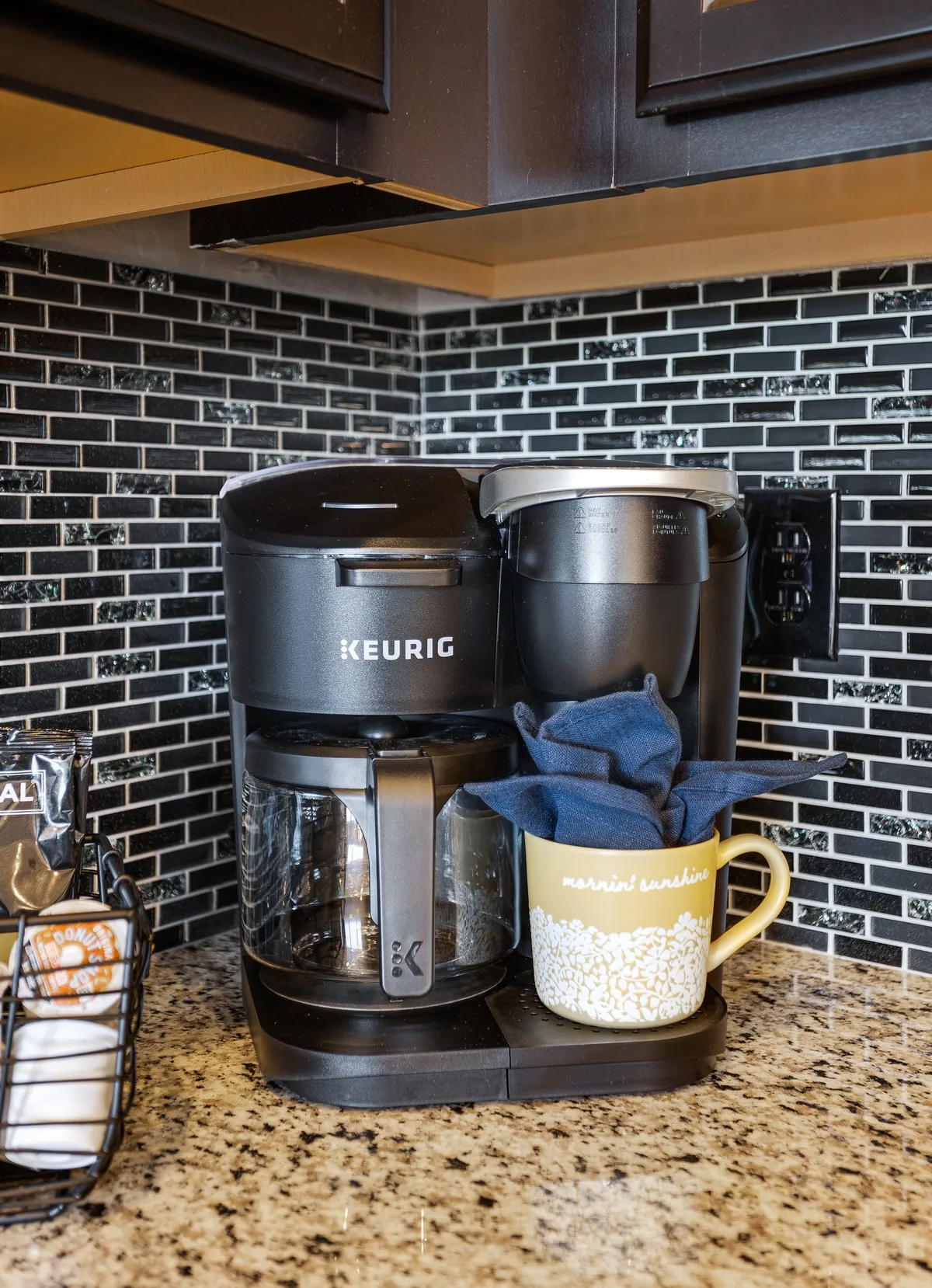 A Keurig coffee maker, transparent coffee pot, and a bright yellow mug are arranged on the counter, highlighting the kitchen’s thoughtful touches for everyday convenience. The close-up composition brings warmth and personality to the space, emphasizing comfort and daily rituals.