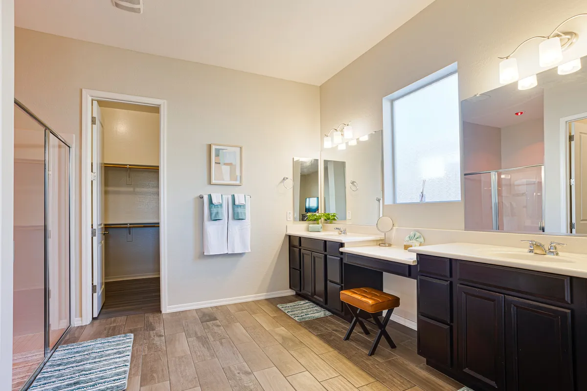 A modern ensuite bathroom featuring a double vanity, expansive mirrors, a walk-in closet, and a spacious shower area. The clean lines and neutral tones create a spa-like, tranquil environment ideal for relaxation and self-care.